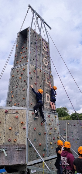 a rock climbing wall with children in helmets and harnesses are climbing
